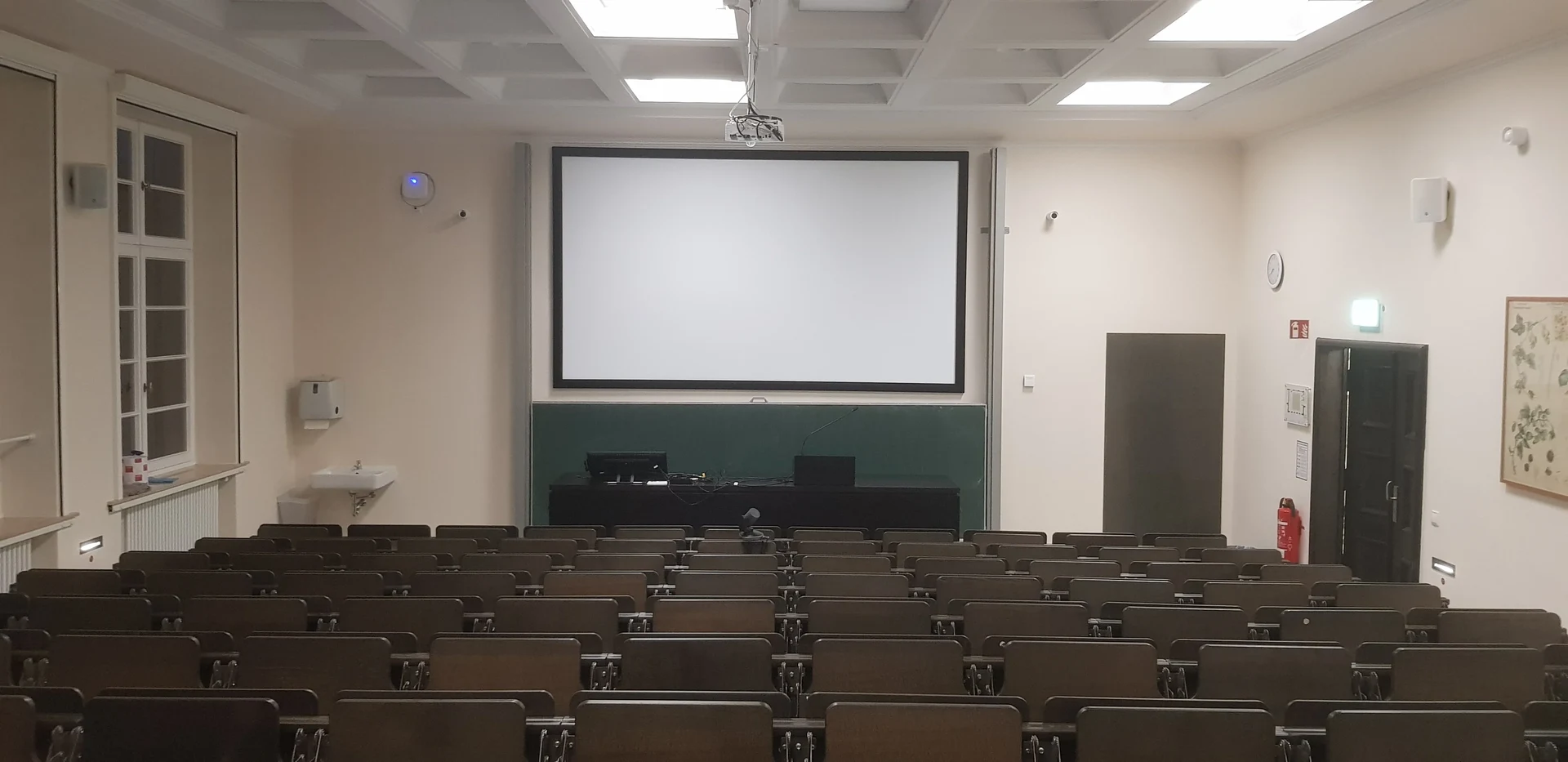 Eine Wissenschaftlerin und ein Wissenschaftler arbeiten hinter einer Glasfassade und mischen Chemikalien mit Großgeräten.